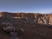 the hikeer is walking along a rocky mountain landscape in the sun set, near to an orange rock cliff and a vast view