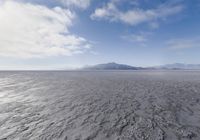 the lone man is walking across the barren area in the distance are mountains, trees, and a hazy blue sky