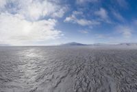 the lone man is walking across the barren area in the distance are mountains, trees, and a hazy blue sky