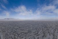 the lone man is walking across the barren area in the distance are mountains, trees, and a hazy blue sky