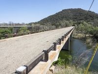 a view from a bridge overlooking trees and a mountain range of hills behind a bridge