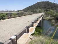 a view from a bridge overlooking trees and a mountain range of hills behind a bridge