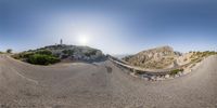 a photo taken in the mirror of a hill top road way with a bridge going around it