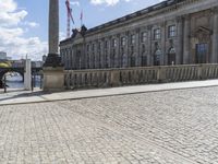 a street view showing several large buildings in a city with cobblestones and people walking around