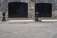 two black fire hydrant sitting in front of a stone building and on the sidewalk is a clock tower