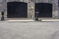 two black fire hydrant sitting in front of a stone building and on the sidewalk is a clock tower