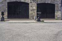 two black fire hydrant sitting in front of a stone building and on the sidewalk is a clock tower