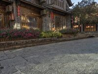 an old street with flowers and a building with red lanterns and stone streets on one side