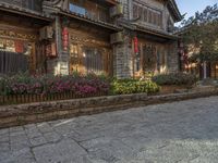 an old street with flowers and a building with red lanterns and stone streets on one side