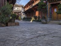 stone courtyard with antique wooden buildings and shrubs in pots on the right side of it