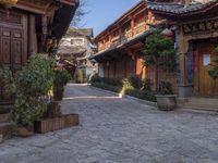 stone courtyard with antique wooden buildings and shrubs in pots on the right side of it