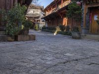 stone courtyard with antique wooden buildings and shrubs in pots on the right side of it