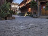 stone courtyard with antique wooden buildings and shrubs in pots on the right side of it