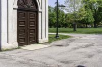 a man is standing next to a large church door near a green field and trees