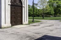 a man is standing next to a large church door near a green field and trees