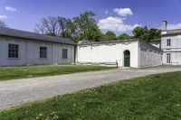 a white building with a green door is next to the grass and walkway between two buildings