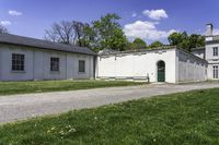 a white building with a green door is next to the grass and walkway between two buildings