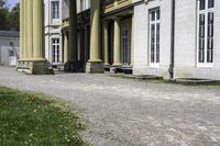 a building with columns is next to a walkway outside of it there are grass and stone in front of the entrance and steps