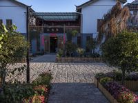 the entrance to an oriental house with a brick walkway and flower beds on either side