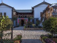 the entrance to an oriental house with a brick walkway and flower beds on either side