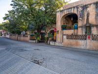 the corner of a street lined with old buildings and plants, along a walkway, between two large green trees