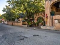 the corner of a street lined with old buildings and plants, along a walkway, between two large green trees