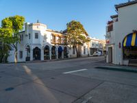 a row of buildings and a small white car on a street corner in the sunlight