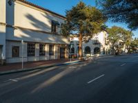 a street view of a sidewalk and some buildings and trees in front of them with a blue sky