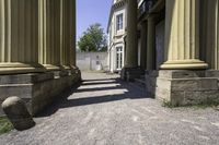 a stone walkway leading to some ancient buildings, with several pillars that are standing alone