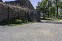 a parking lot with a fence and two barns in the background and trees in the foreground