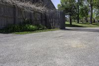 a parking lot with a fence and two barns in the background and trees in the foreground