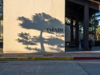 a fire hydrant casting a shadow on a building that reads seventh station on it