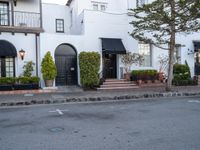 a white apartment building is pictured with potted plants and a street light in front of it