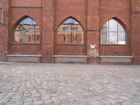 a brick courtyard with windows and benches on the ground, near it is an old building