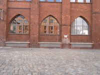 a brick courtyard with windows and benches on the ground, near it is an old building