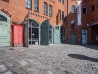 a cobblestone street with red and green doors leading to the entrance of an historic building