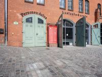 a cobblestone street with red and green doors leading to the entrance of an historic building