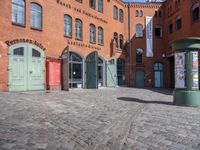 a cobblestone street with red and green doors leading to the entrance of an historic building