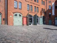 a cobblestone street with red and green doors leading to the entrance of an historic building