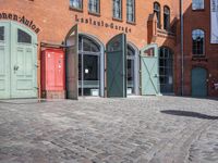 a cobblestone street with red and green doors leading to the entrance of an historic building