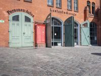 a cobblestone street with red and green doors leading to the entrance of an historic building