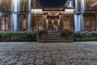 an outdoor entrance to a building lit up at night with lights shining on the windows and a brick walkway