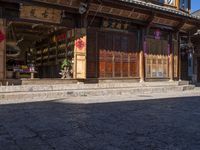 a chinese style store with wooden doors and windows in the sun, with a bricked sidewalk in front