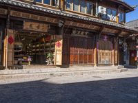 a chinese style store with wooden doors and windows in the sun, with a bricked sidewalk in front