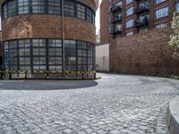 a circular building with two large windows next to some people in the street by some brick buildings