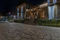 a photo at night with the lights on a street in front of a building and bushes