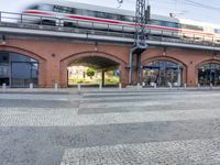 red bricks and an electric train passing by it on a bridge over water and road