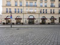 people walking on sidewalk in front of an old hotel building with large windows and doors