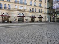 people walking on sidewalk in front of an old hotel building with large windows and doors