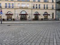 people walking on sidewalk in front of an old hotel building with large windows and doors